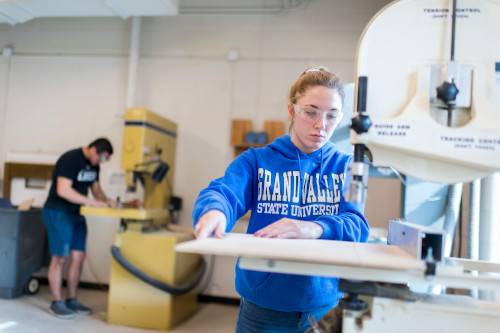 3D Design student wearing blue GVSU sweatshirt and working on a bandsaw at a Woodshop